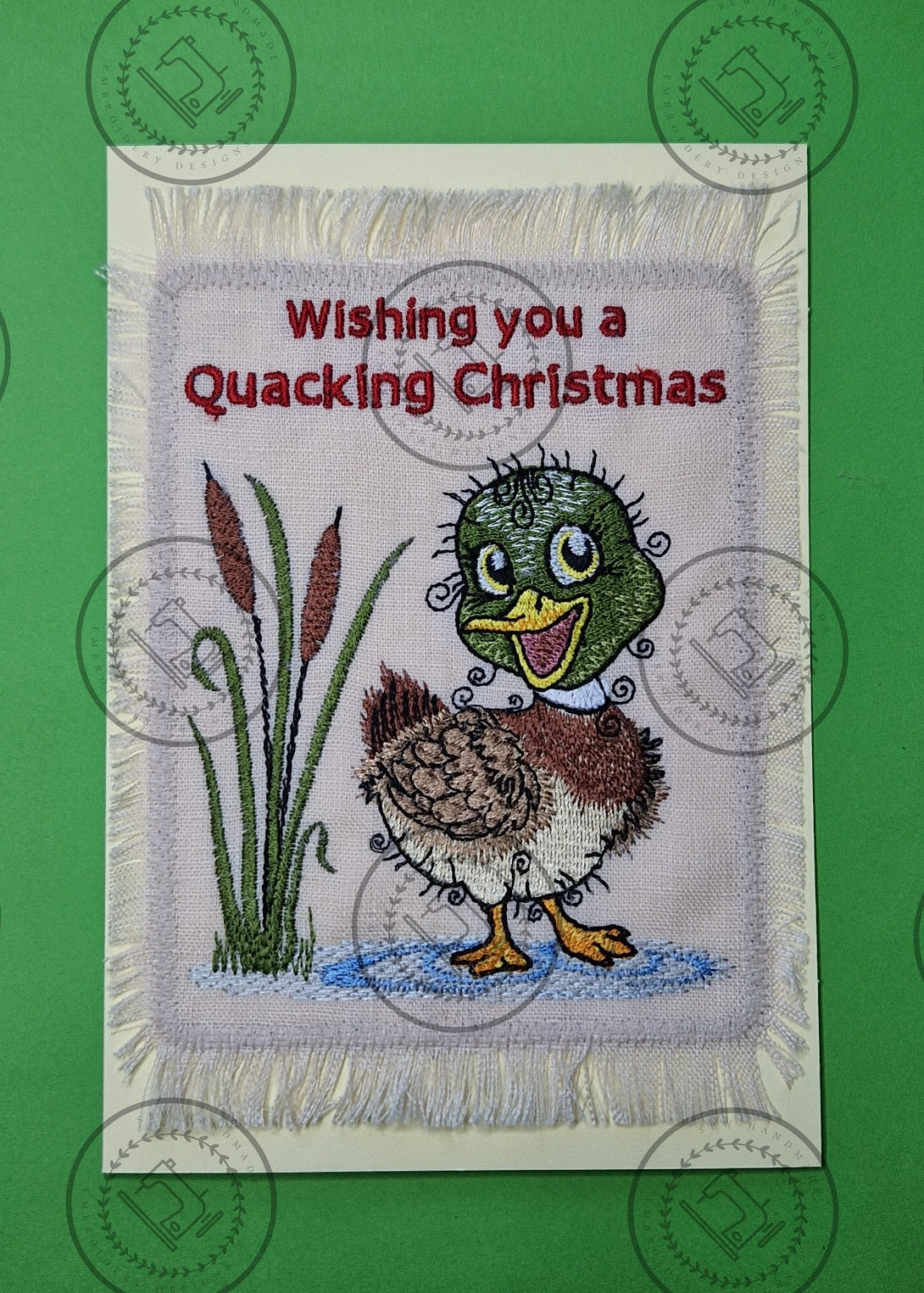 "An embroidered design of a cheerful mallard duck with a vibrant green head, brown and beige body, and yellow beak. The duck is standing in a small blue puddle next to tall cattail reeds, with a whimsical and curly detailing style."