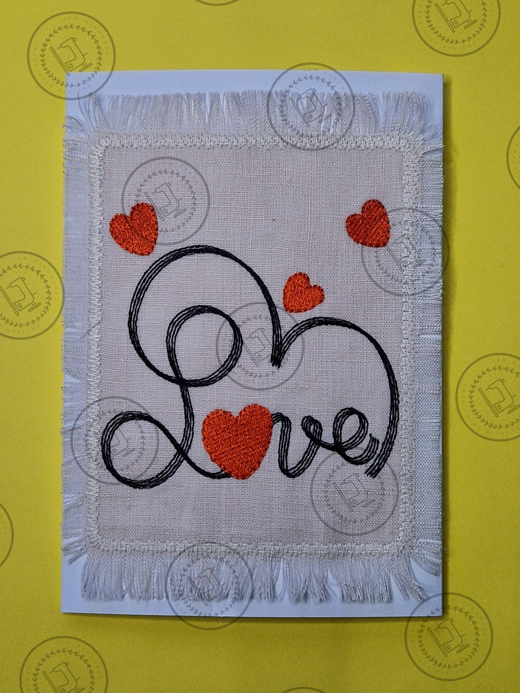 "An embroidered design featuring the word 'Love' in cursive script, stitched with black thread. The letter 'o' is shaped like a red heart, and additional red hearts are scattered decoratively around the design on a light fabric background."
